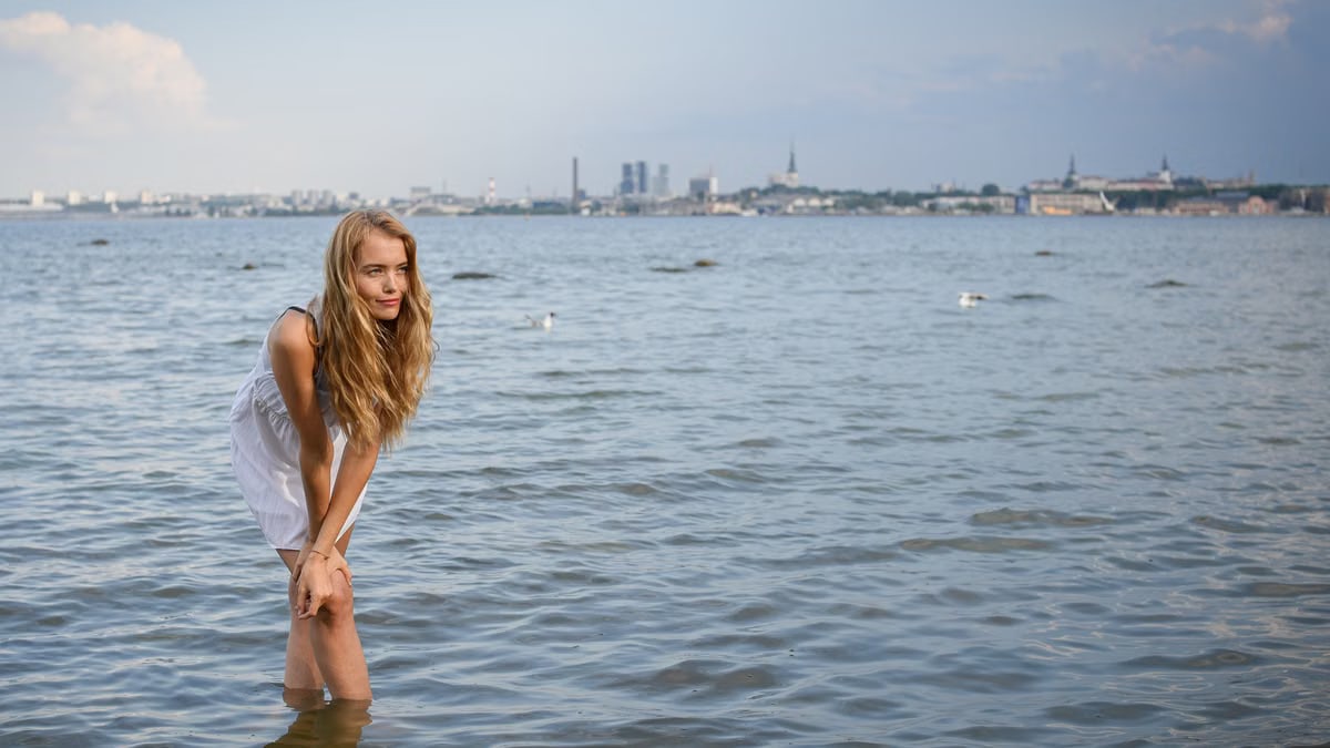 Young woman standing in water with Tallinn skyline in the background on a sunny day.